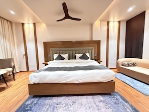 A modern hotel room with a wooden bed, a sofa, a desk, and a ceiling fan. - TRINITY PALACE (Chas)
