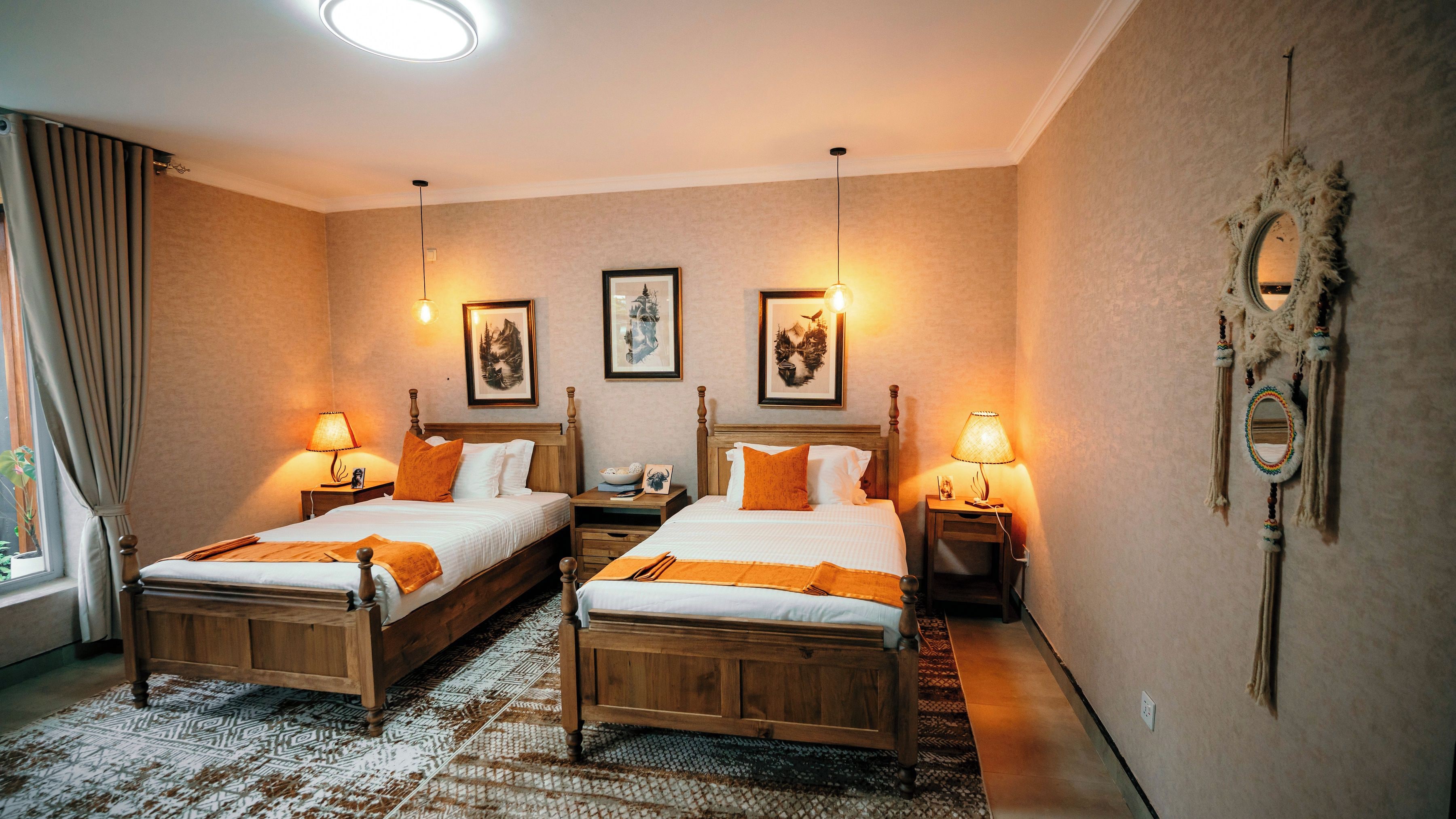 Ein Hotelzimmer mit zwei Holzbettgestellen, einem gemusterten Teppich und gerahmten Kunstwerken an den Wänden.