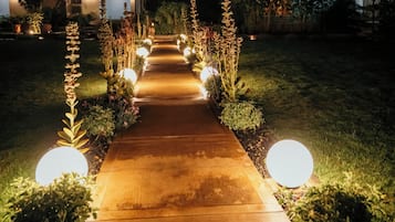 Un camino conduce a un edificio de diseño moderno, rodeado de jardines cuidados e iluminado por luces esféricas.