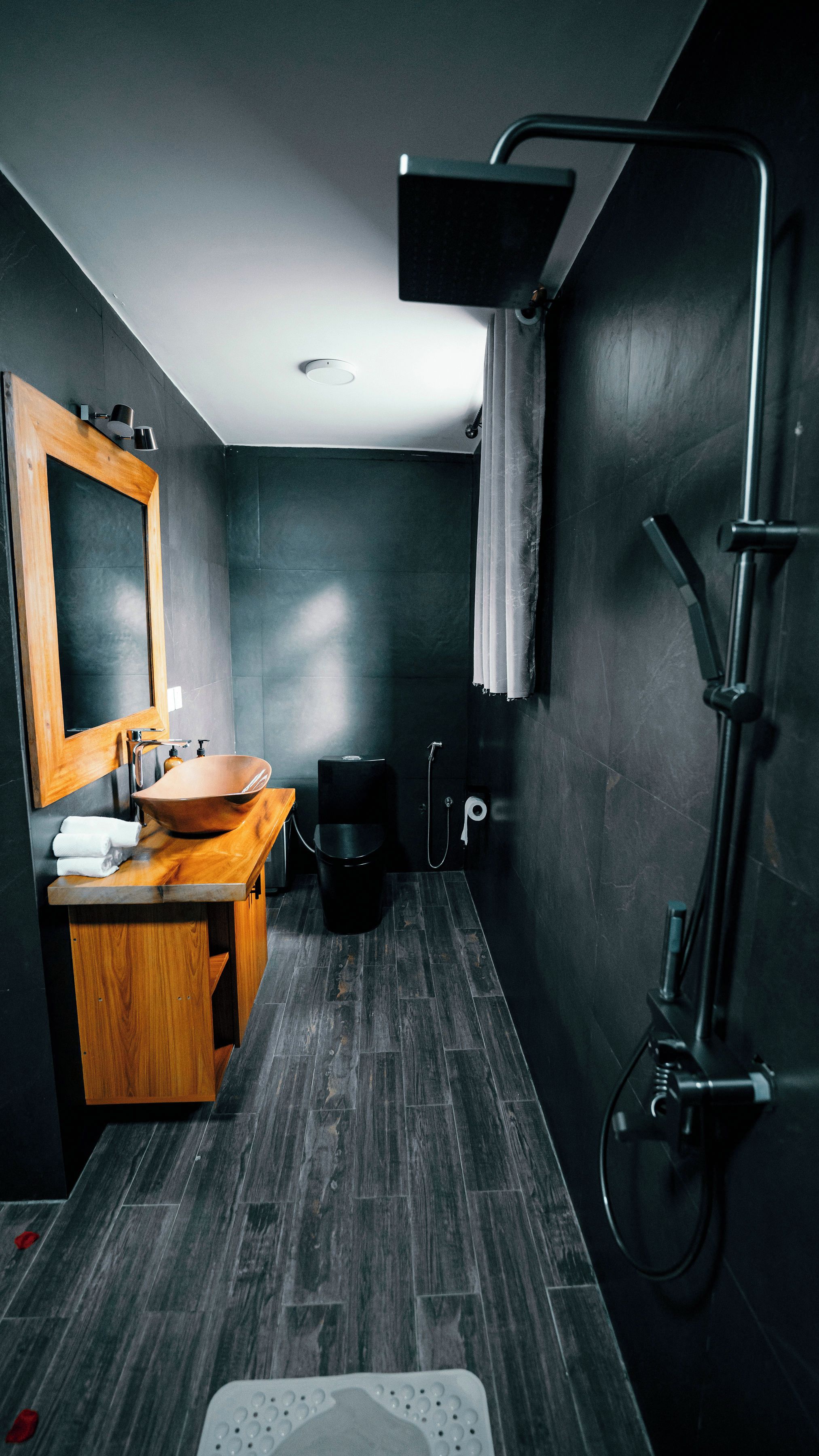 A modern bathroom with a wooden vanity, a large mirror, a vessel sink, a shower, and a towel rack.