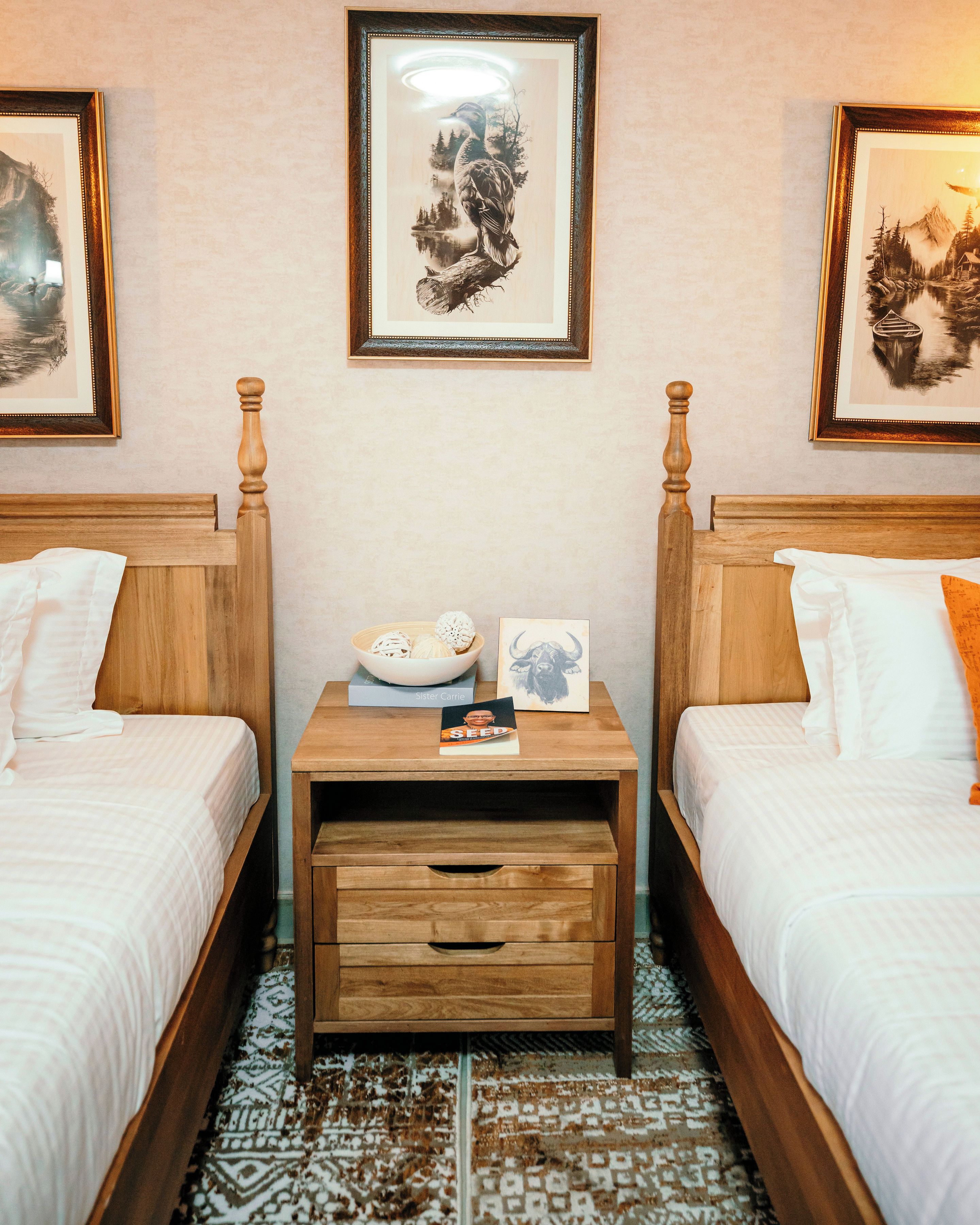 A hotel room with two beds, a nightstand with a bowl of fruit, and framed artwork on the walls.