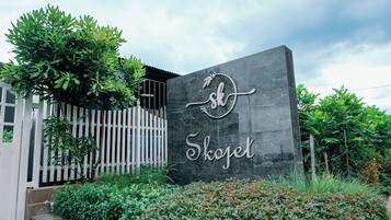 A sign with the name 'Skogel' on a dark stone wall, surrounded by greenery and a white fence.