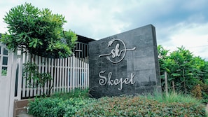 A sign with the name 'Skogel' on a dark stone wall, surrounded by greenery and a white fence.