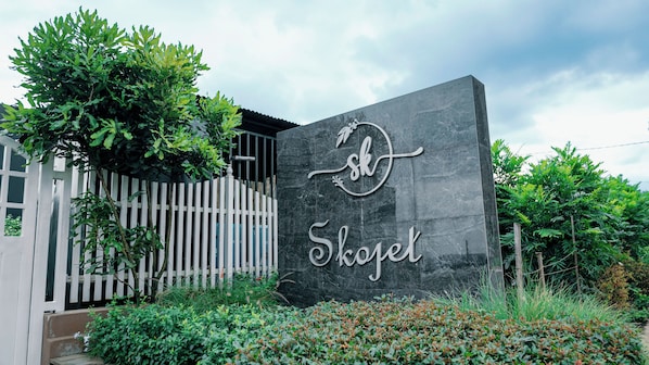 A sign with the name 'Skogel' on a dark stone wall, surrounded by greenery and a white fence. - skojet boutique hotel (Cyuve)