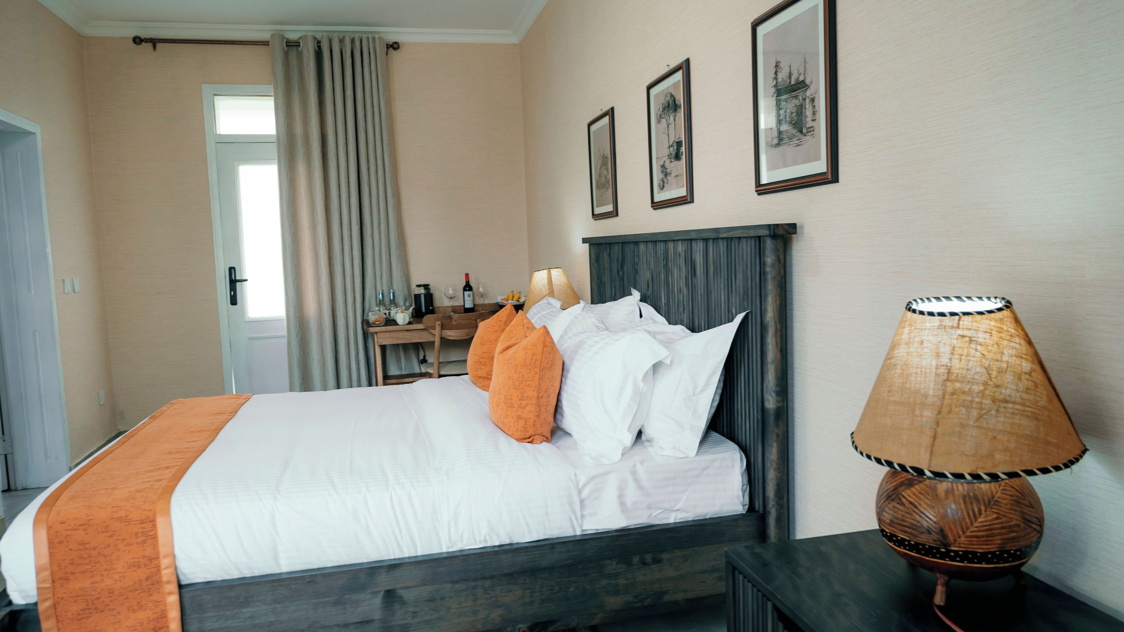 Una habitación de hotel con una cama, una lámpara de noche, un escritorio con una silla y una ventana con cortinas.