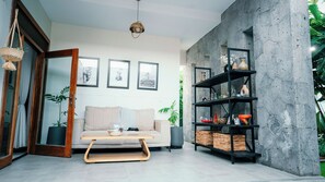 A modern living room with a sofa, coffee table, and a bookshelf against a concrete wall. - skojet boutique hotel (Cyuve)