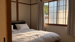A bedroom with a bed, a window with curtains, and a view of the outside.