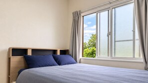 A bedroom with a bed, a window with curtains, and a view of greenery outside.