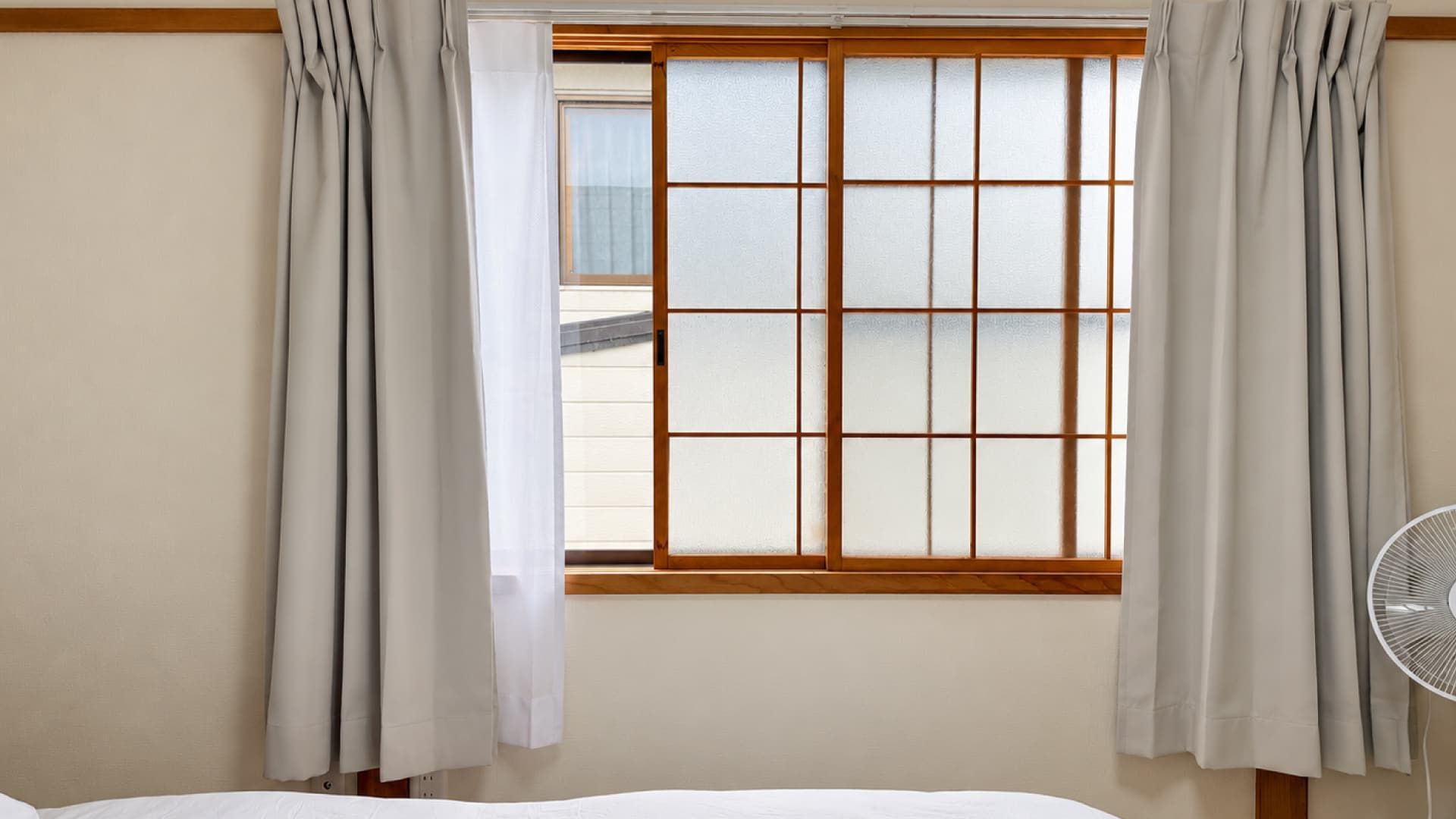 A room with a bed, a window with wooden frames, and a fan.