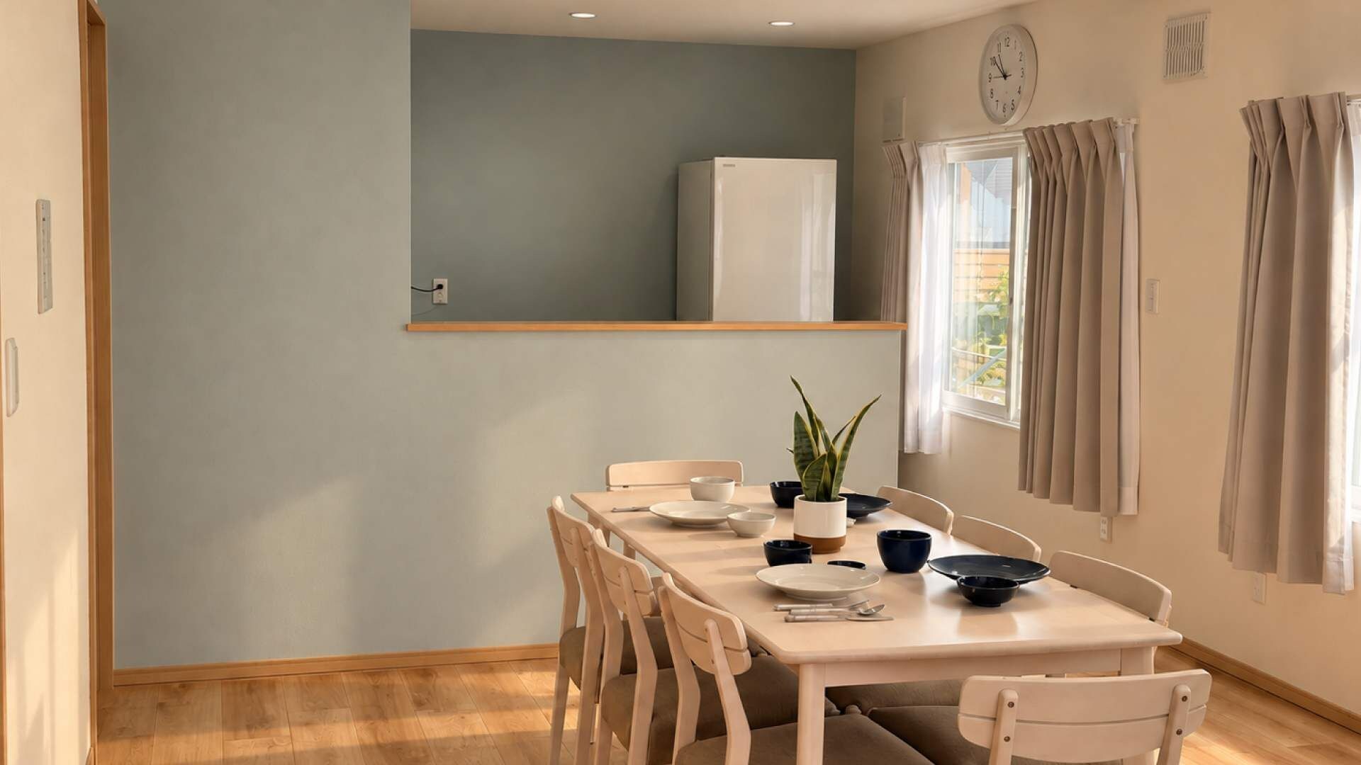 A dining area with a table set for two, chairs, a potted plant, and a clock on the wall.