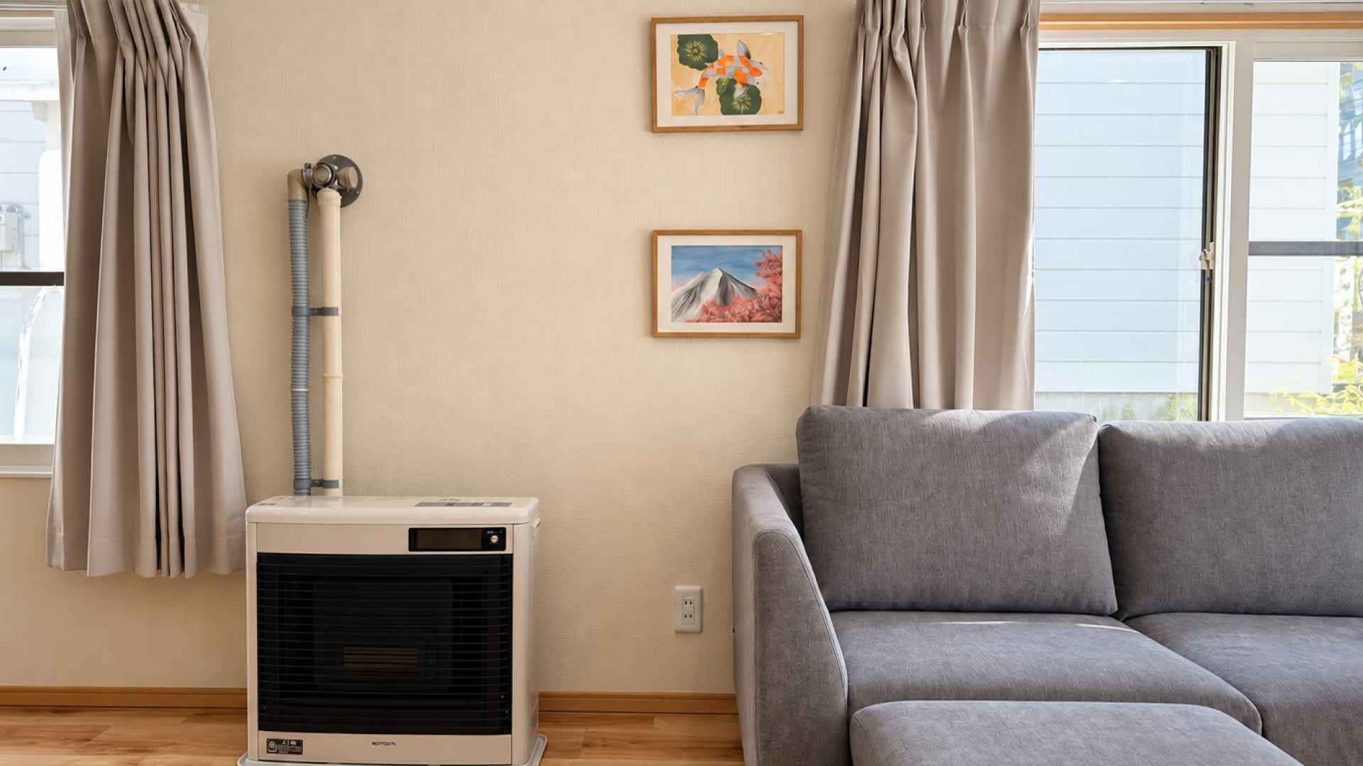A room with a gray sofa, a wall-mounted air conditioner, and two framed pictures.