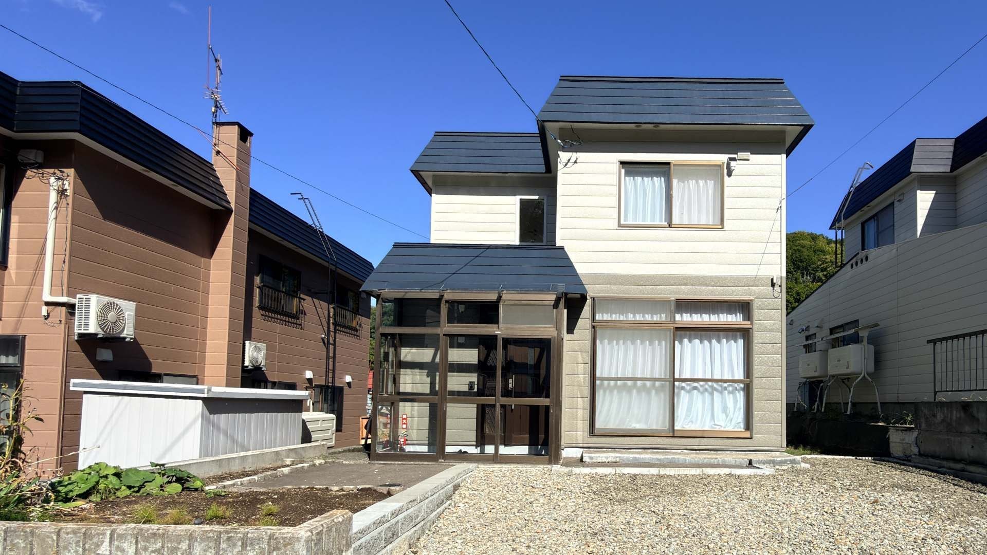 A two-story building with a central entrance, large windows, and a gravel driveway.