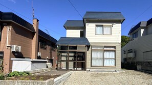 A two-story building with a central entrance, large windows, and a gravel driveway.