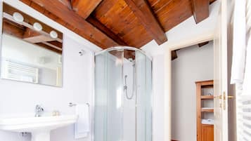 Een badkamer met een douchecabine van glas, een witte wastafel en een houten plafond.