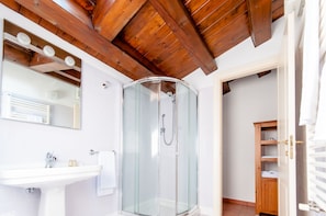 A bathroom with a glass-enclosed shower, a white sink, and a wooden ceiling. - Il Giardinetto Rooms  (Ferrara)