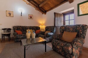 A living room with floral-patterned sofas, a glass coffee table, and a wooden ceiling. - Casa del Guarda - Finca & Spa Vereda Real (Albacete)