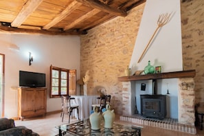 A rustic interior with exposed brick walls, a wooden ceiling, a television, a fireplace, and a dining area.