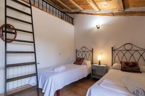 A room with two beds, a ladder, a nightstand, and a wall-mounted light fixture.