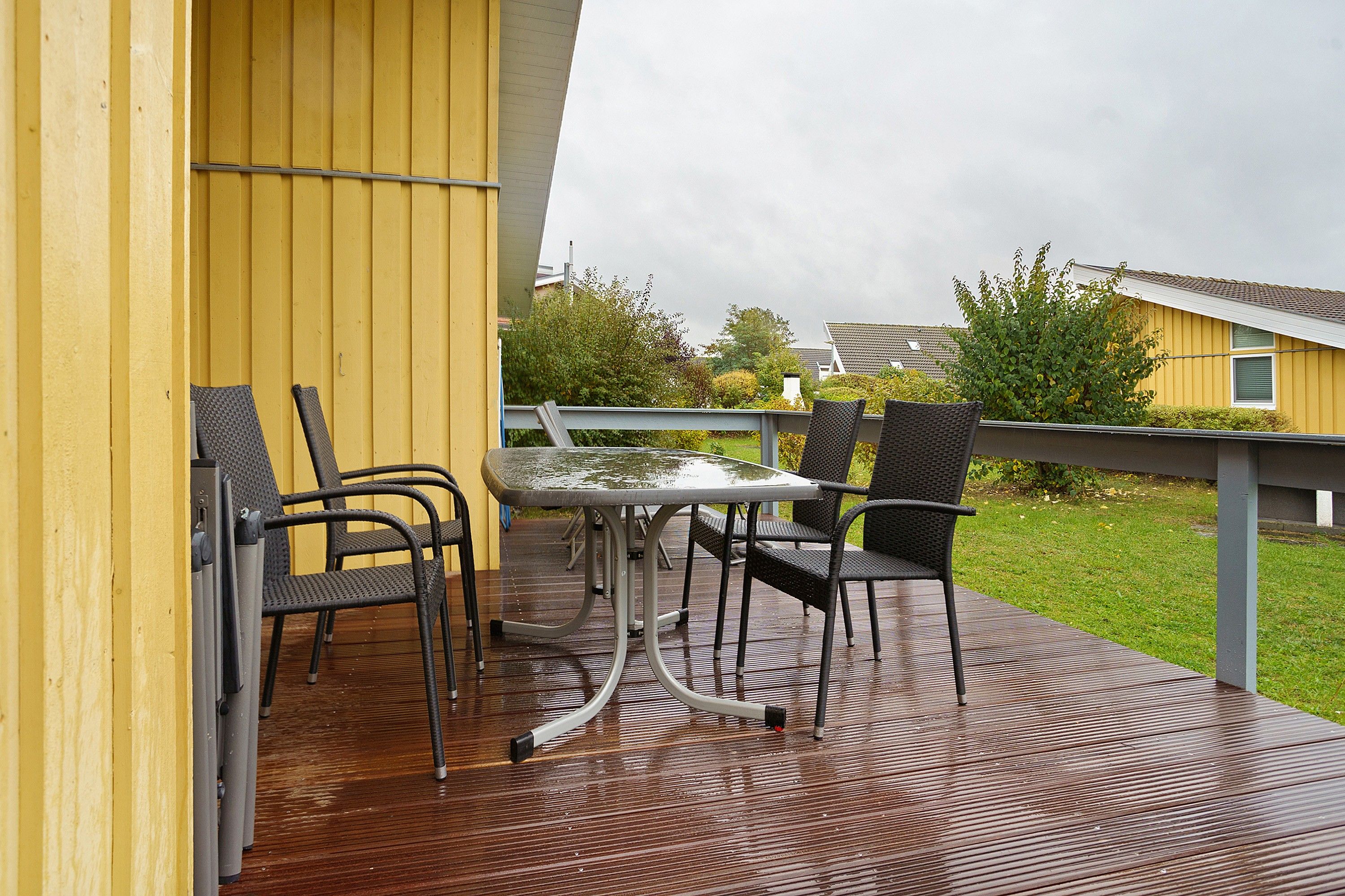 Una terraza con una mesa y sillas, piso de madera y un edificio amarillo al fondo.