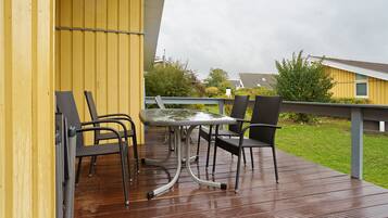 Una terraza con una mesa y sillas, piso de madera y un edificio amarillo al fondo.
