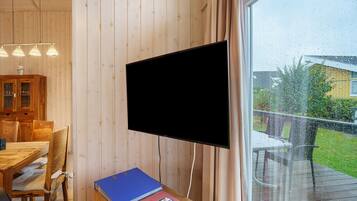 Huoneessa on seinälle asennettu televisio, ruokapöytä tuoleineen ja ikkunasta avautuva näkymä ulos.