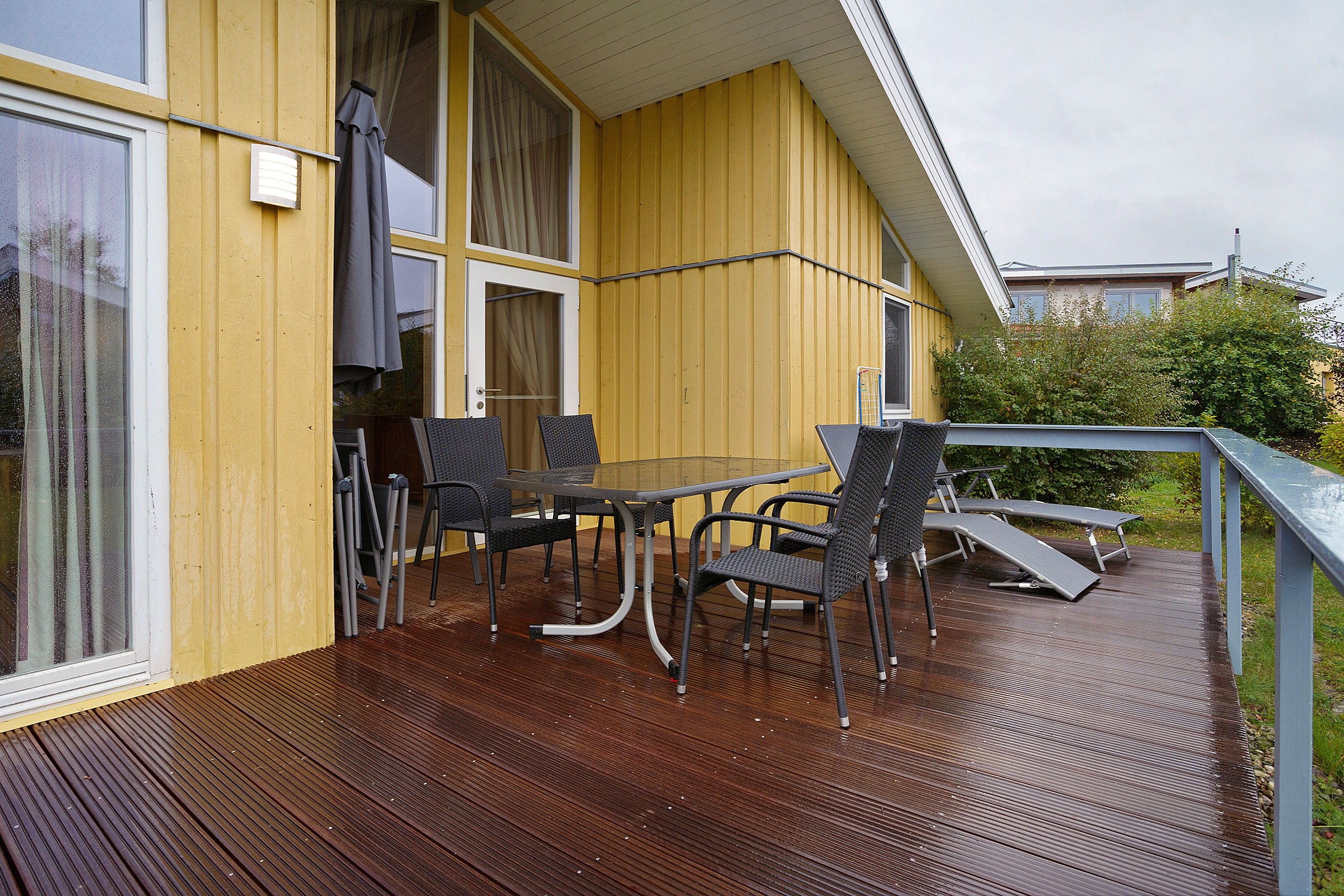Eine Holzterrasse mit Tisch und Stühlen, einer Schiebetür und einem Fenster.