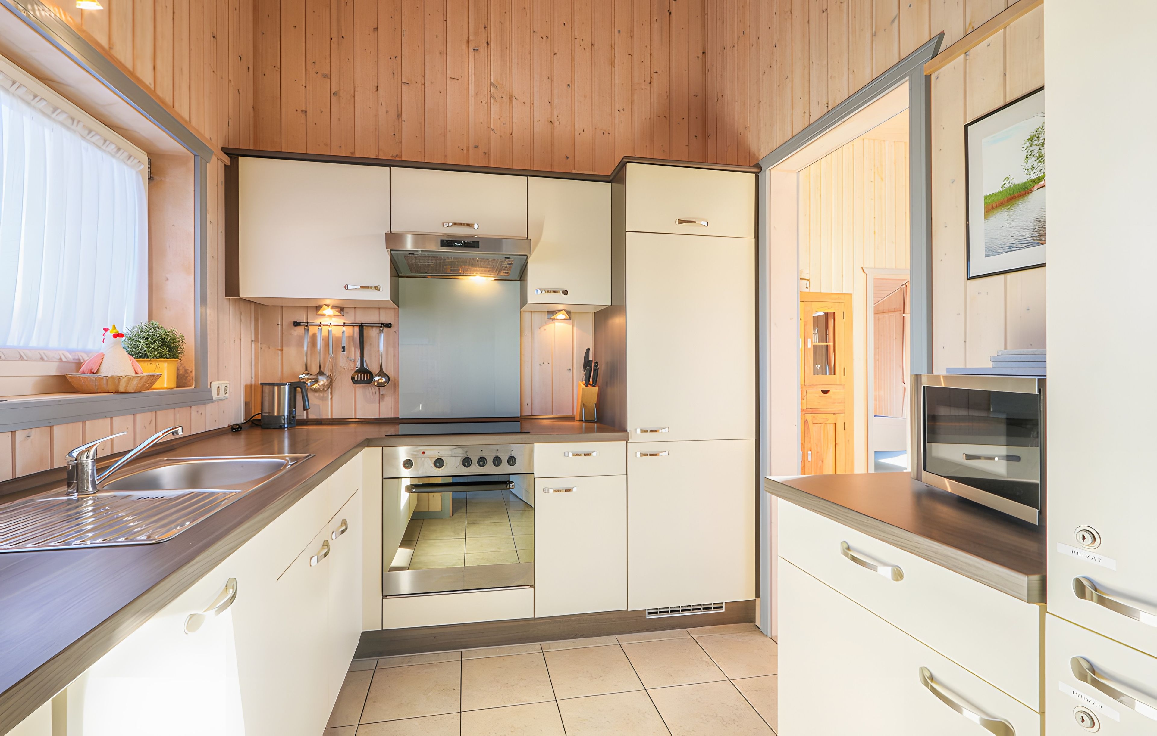 A compact kitchen with a stove, oven, and sink, wooden cabinets, and a window with blinds.