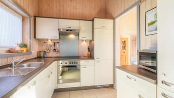 A compact kitchen with a stove, oven, and sink, wooden cabinets, and a window with blinds.