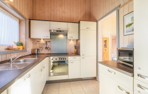 Una cocina compacta con estufa, horno y pileta, muebles de madera y una ventana con persianas.