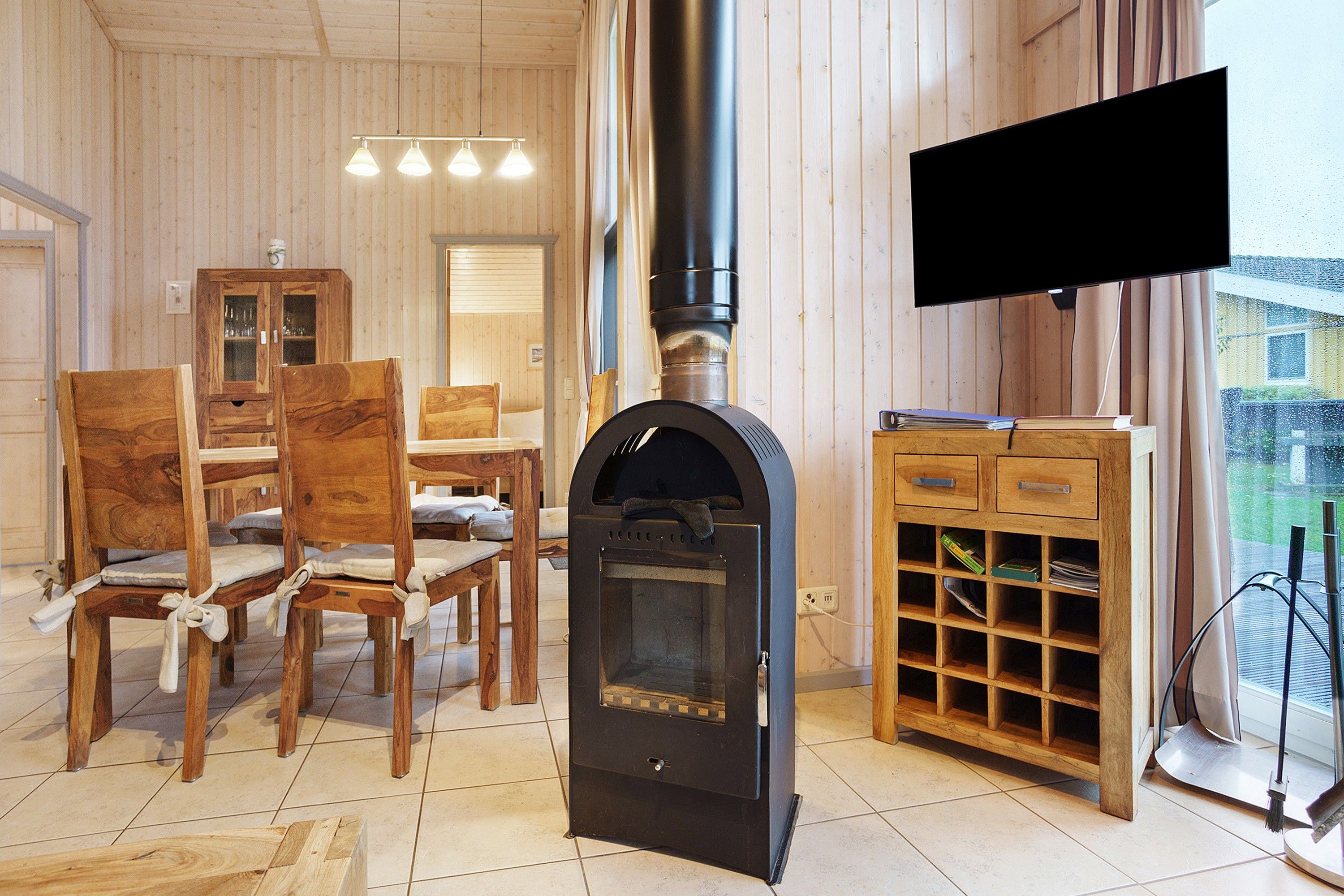Ein Zimmer mit Kamin, Holzmöbeln, einem Fernseher und Blick ins Freie.