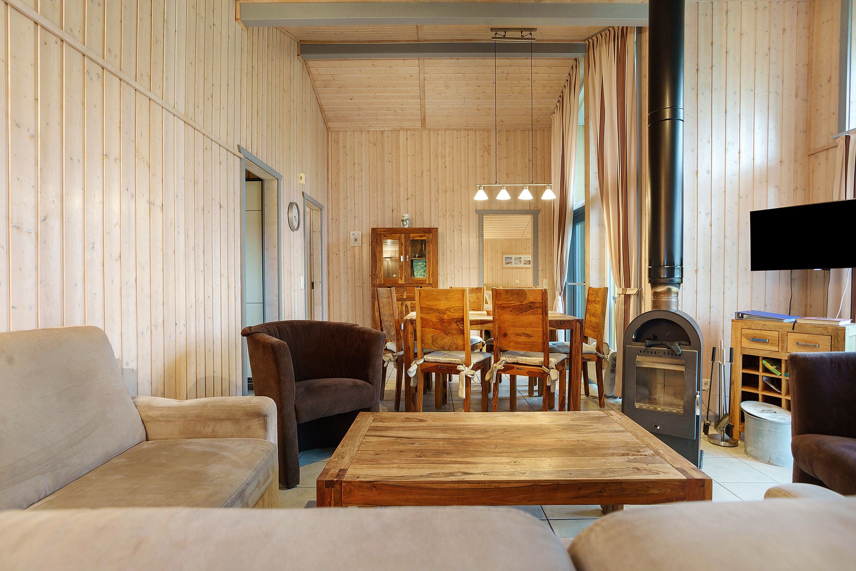 A cozy living room with wooden walls, a sofa, chairs, a coffee table, and a fireplace.