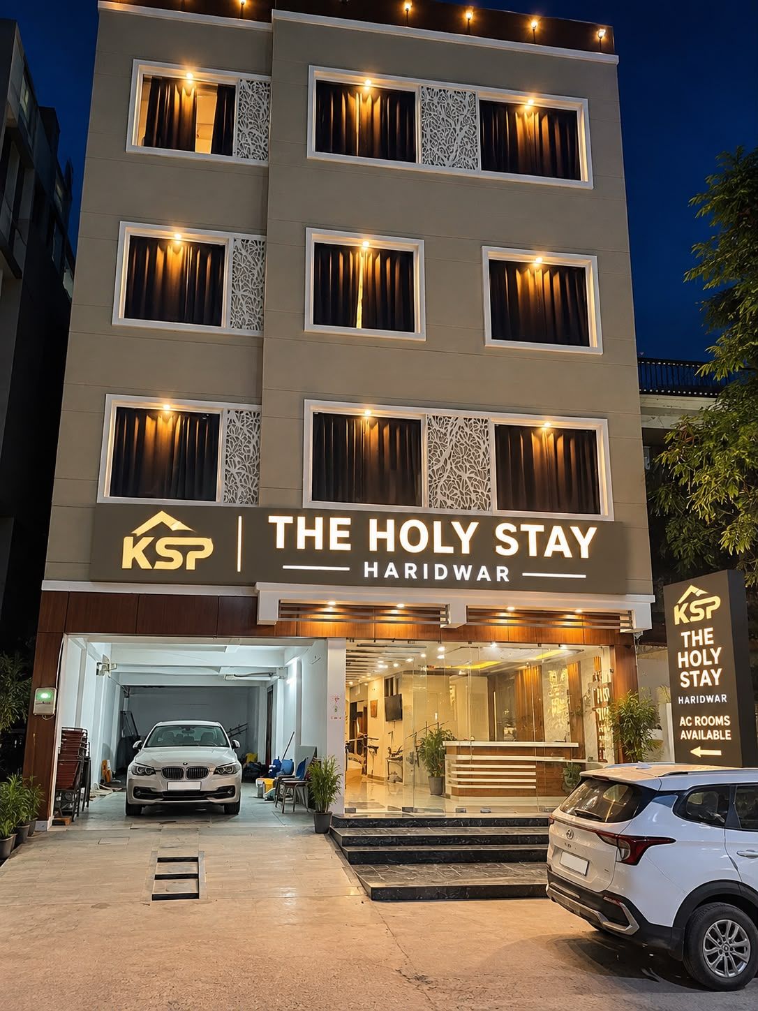 Ett hotell som heter ”The Holy Stay” med en modern fasad, flera fönster med gardiner och en skylt som visar att det finns rum med luftkonditionering.