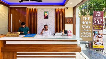 Un comptoir d’accueil d’hôtel avec un guichet d’enregistrement, un ventilateur de plafond et un panneau publicitaire pour les chambres climatisées.