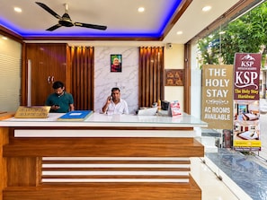 Una recepción de hotel con mostrador de registro, un ventilador de techo y un letrero que anuncia habitaciones con aire acondicionado.