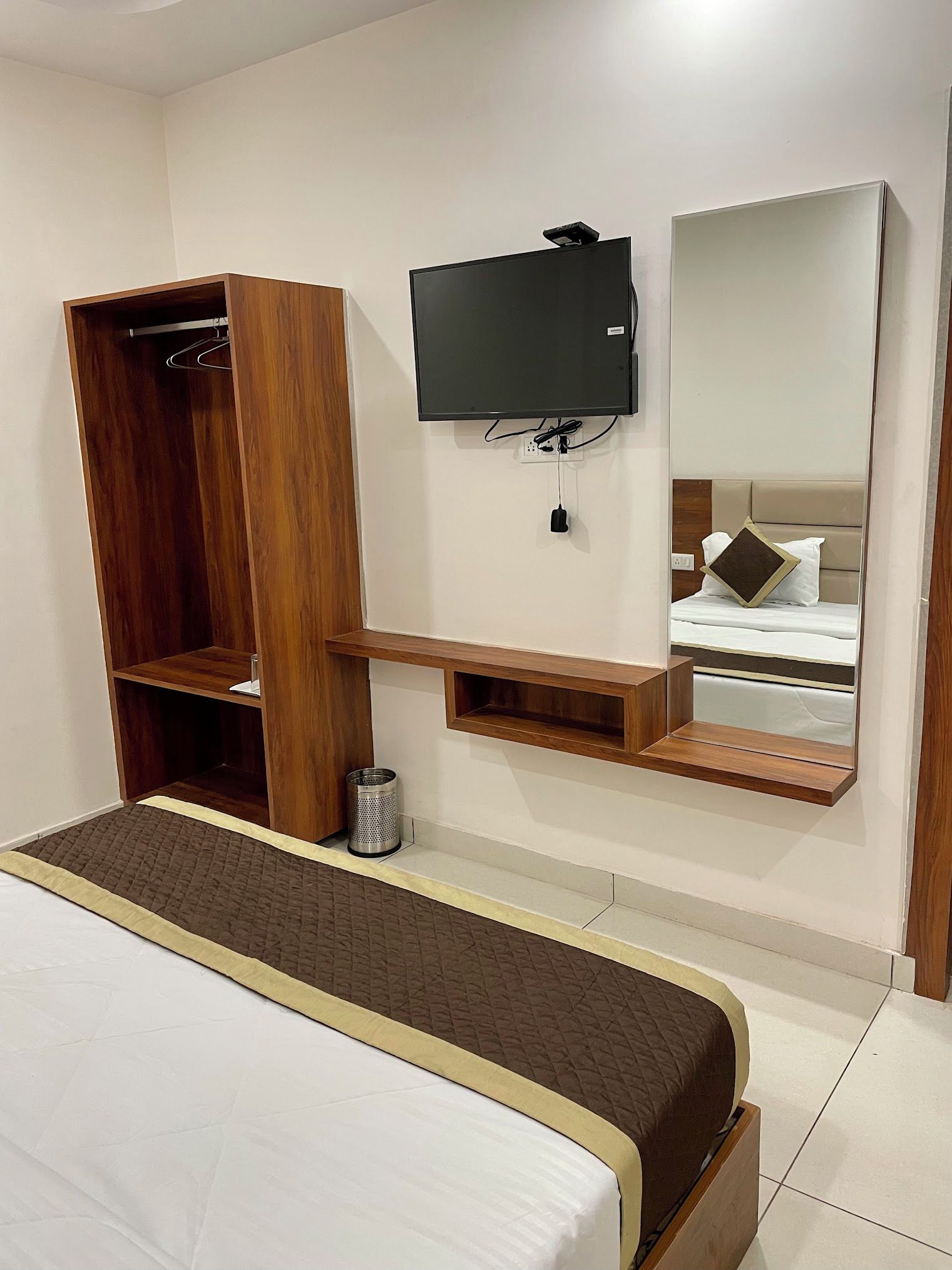 Una habitación de hotel con una cama, un armario de madera, un televisor montado en la pared y un espejo que refleja la cama.