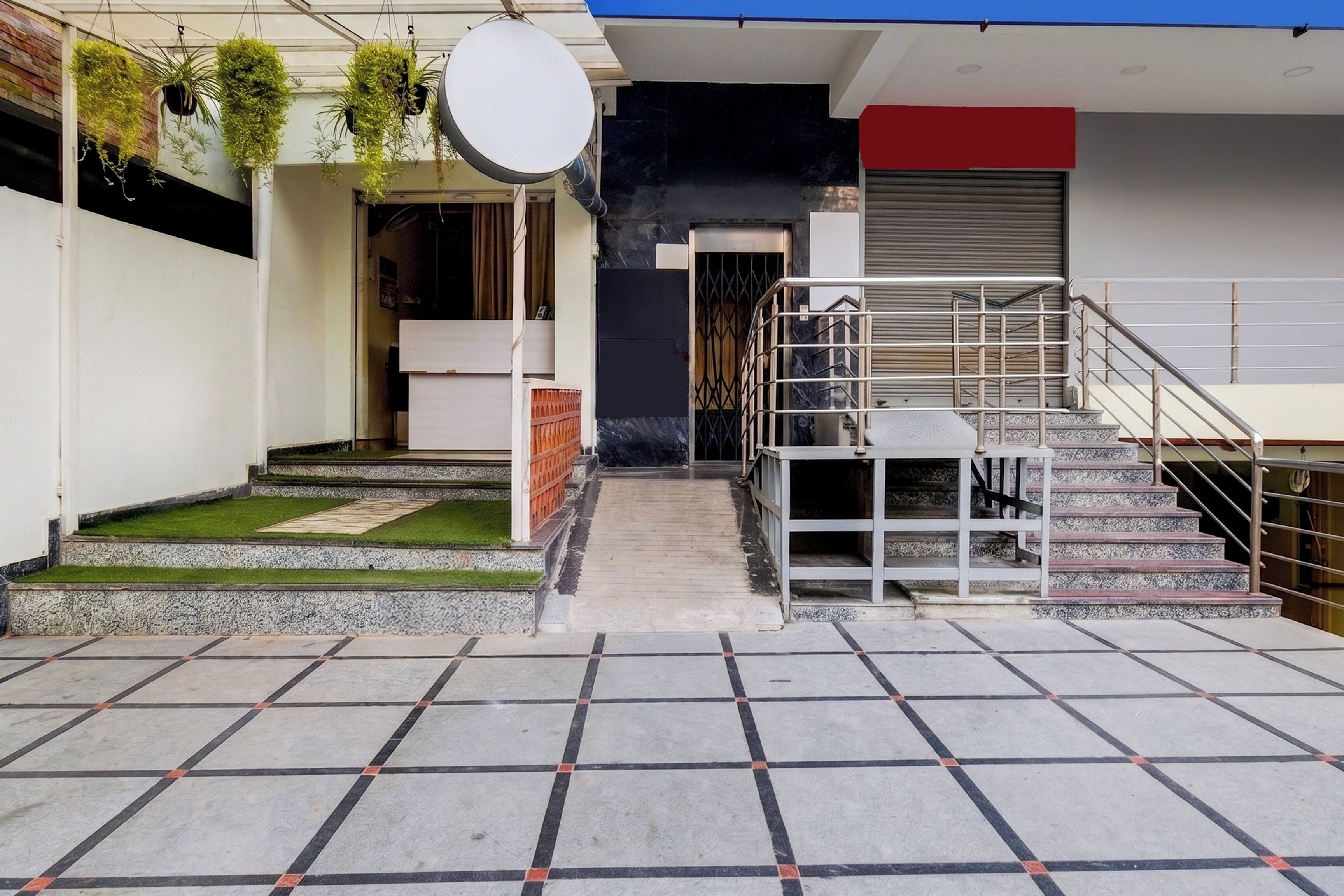 Entrada de un edificio con una escalera, un pequeño jardín y una barandilla de metal.