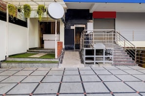 Entrada de um edifício com escadas, um pequeno jardim e um guarda-corpo de metal.