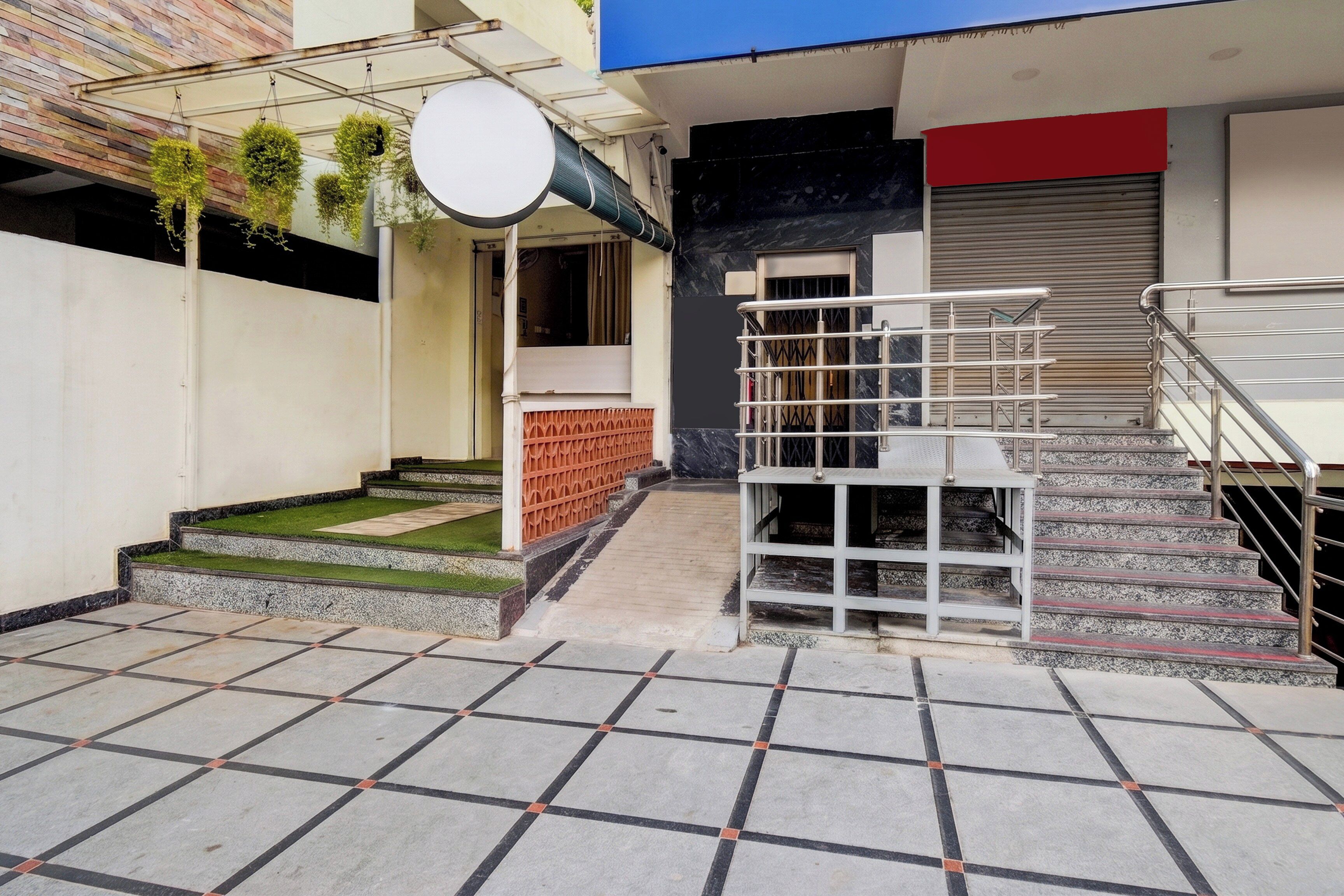 Um edifício com escadaria, área coberta com plantas pendentes e entrada gradeada.