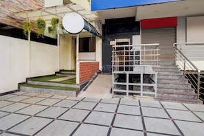 Um edifício com escadaria, área coberta com plantas pendentes e entrada gradeada.