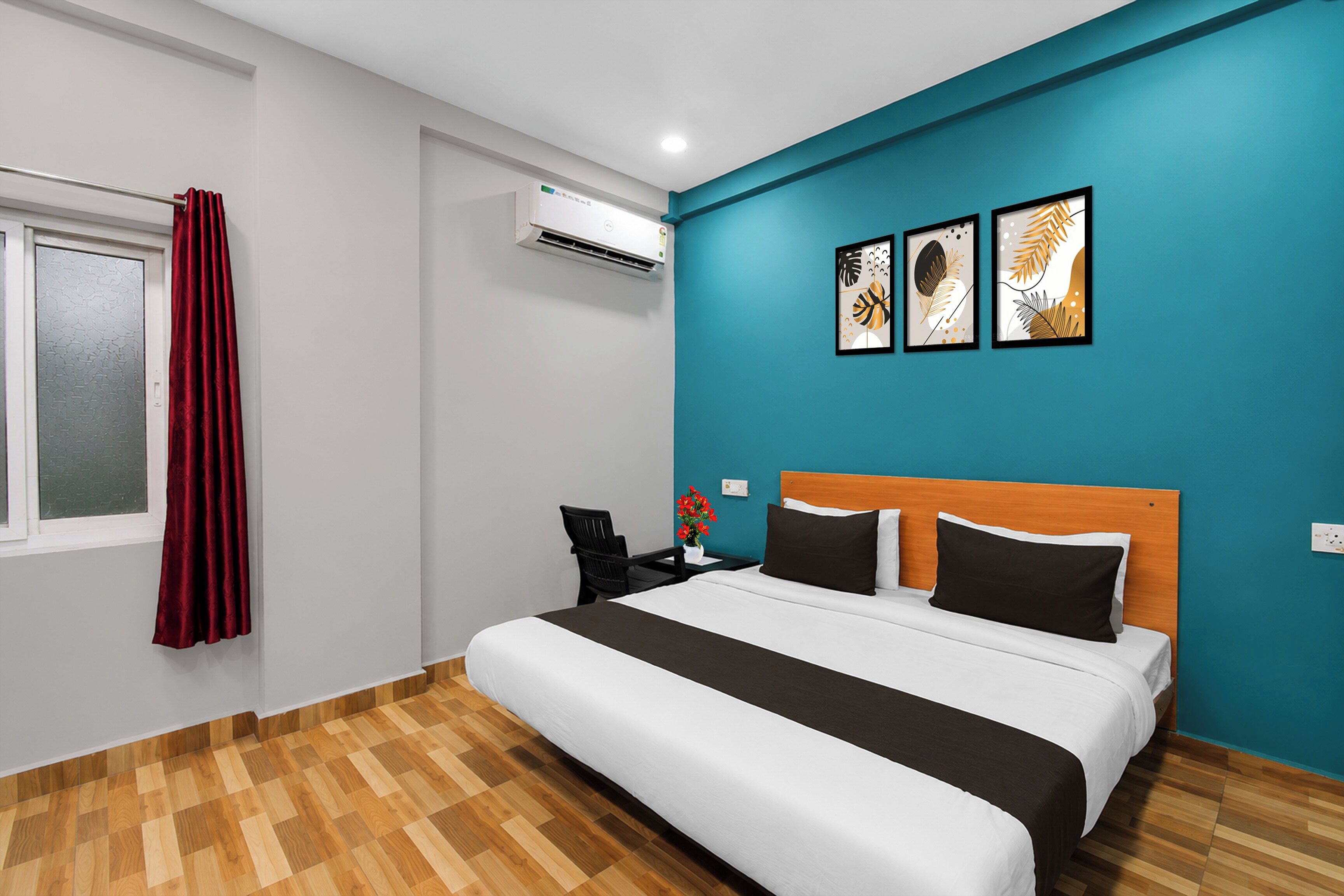 Quarto de hotel com uma cama, mesa de cabeceira, cortina vermelha, aparelho de ar condicionado e duas obras de arte na parede.