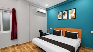Quarto de hotel com uma cama, mesa de cabeceira, cortina vermelha, aparelho de ar condicionado e duas obras de arte na parede.