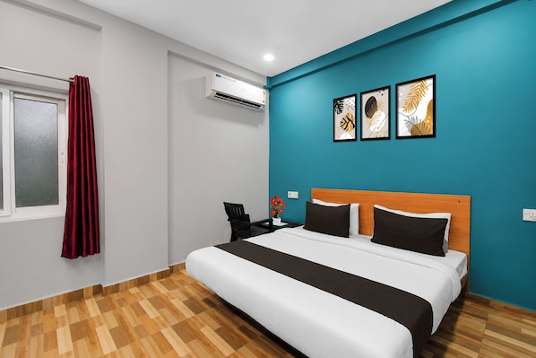 Quarto de hotel com uma cama, mesa de cabeceira, cortina vermelha, aparelho de ar condicionado e duas obras de arte na parede.
