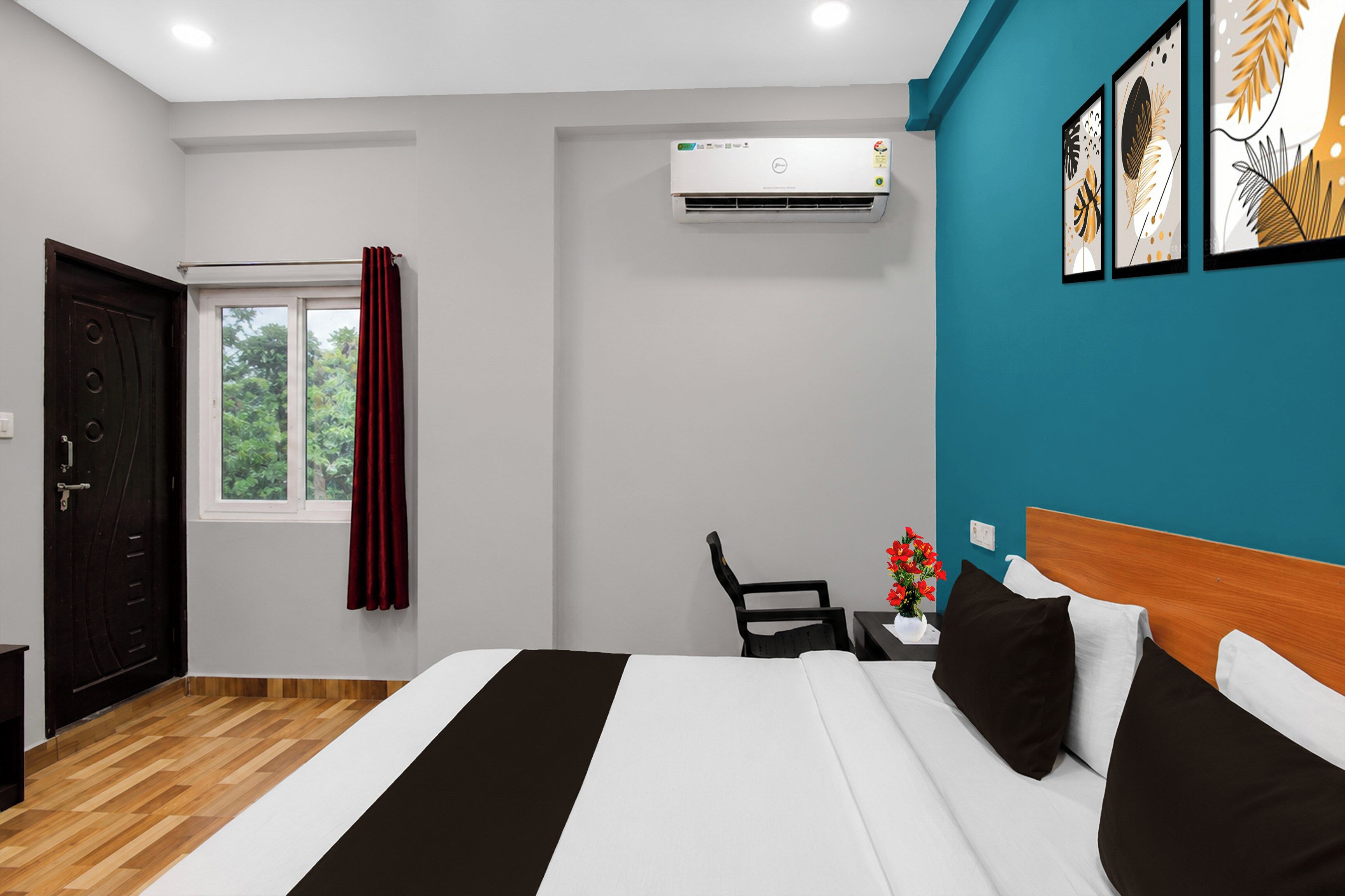 Habitación de hotel con cama, escritorio con silla, equipo de aire acondicionado, ventana con cortinas y una obra de arte en la pared.