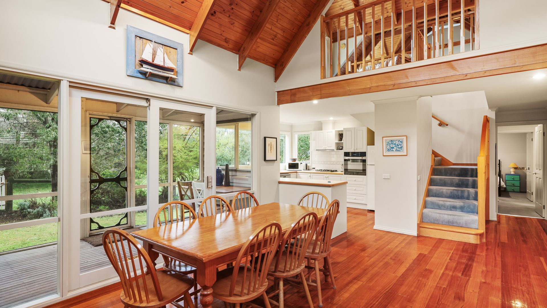 A spacious dining area with a wooden table and chairs, a kitchen with white cabinets, and a staircase leading to an upper level.