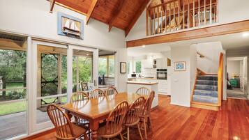A spacious dining area with a wooden table and chairs, a kitchen with white cabinets, and a staircase leading to an upper level.