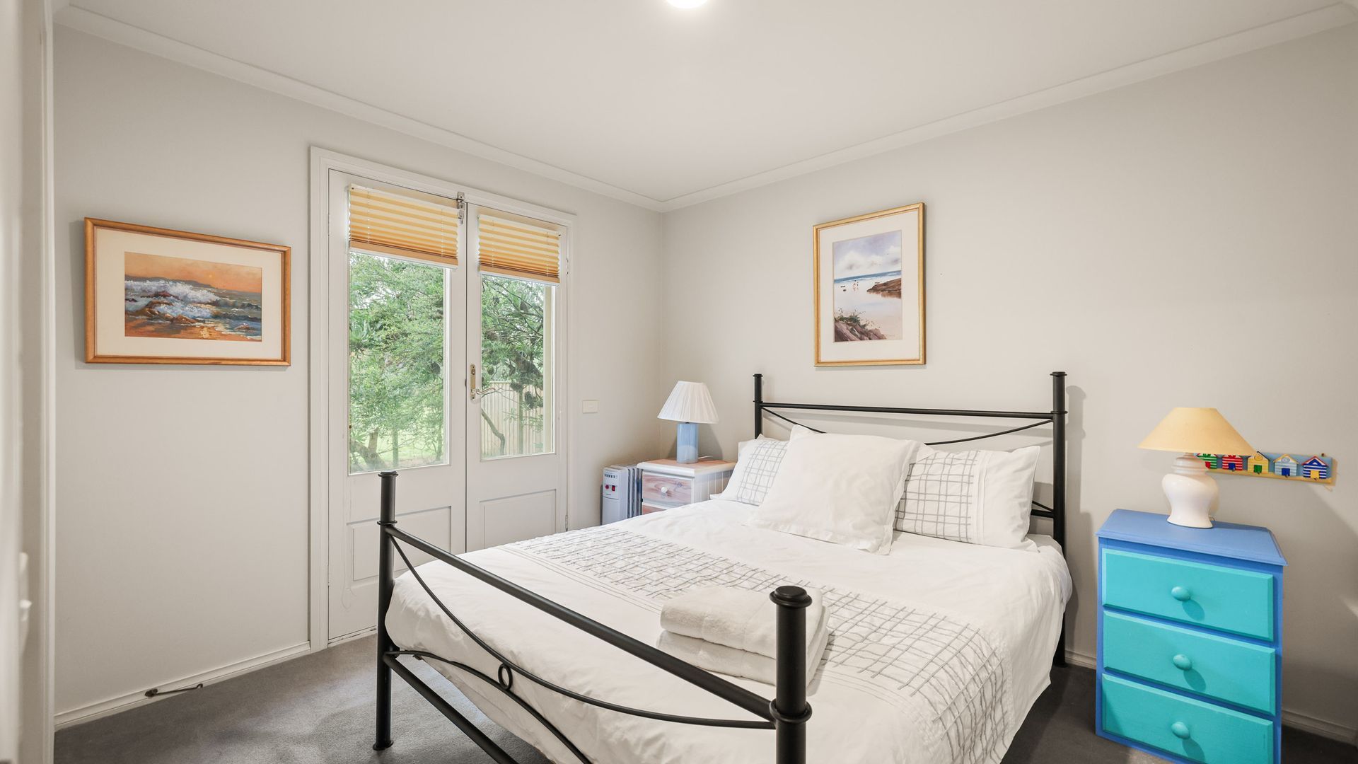 A bedroom with a bed, bedside tables, a dresser, and two windows with blinds.
