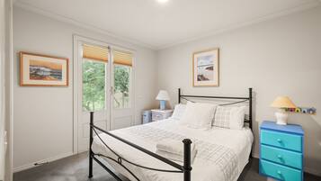 A bedroom with a bed, bedside tables, a dresser, and two windows with blinds.