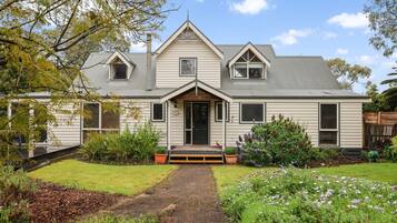 A two-story house with a front porch, a chimney, and a well-maintained garden with various plants and flowers.