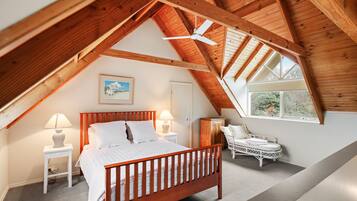 A bedroom with a sloped ceiling, a bed, bedside lamps, a chair, and a window.