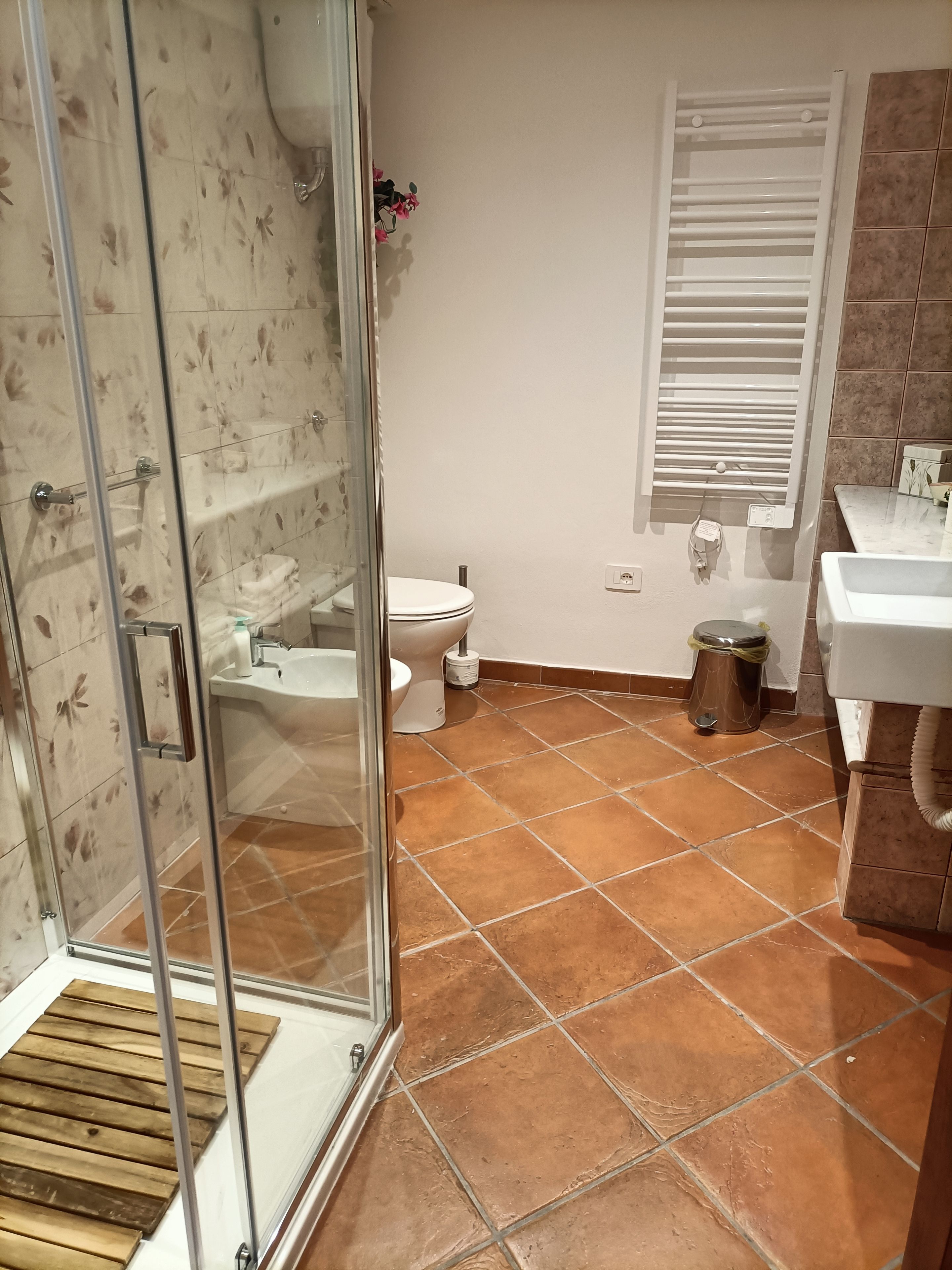 A bathroom with a glass shower enclosure, a toilet, a sink, and a window with blinds.